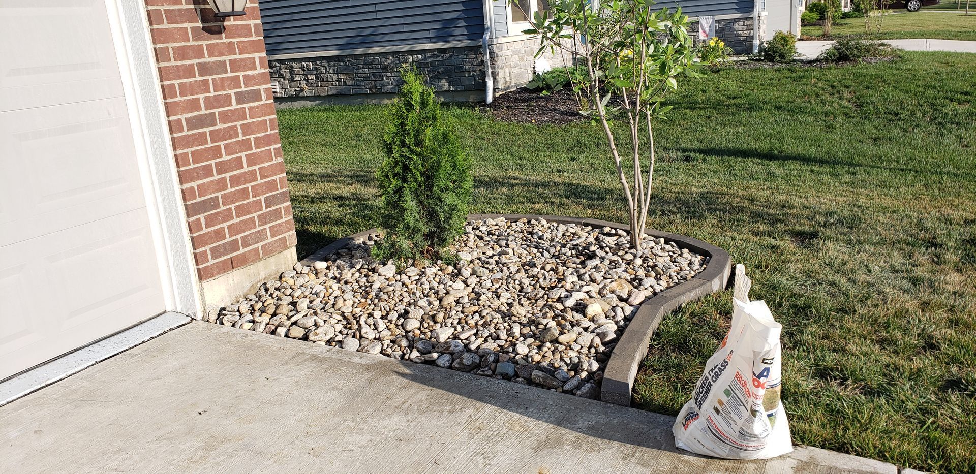 A bag of rocks is sitting on the sidewalk in front of a house.