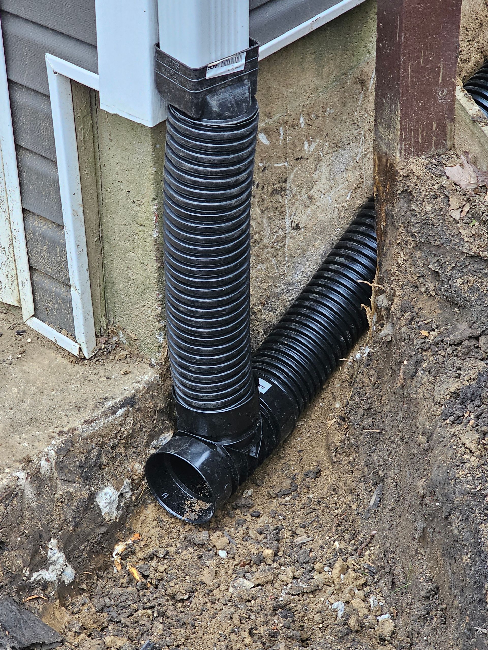 A black drain pipe is sitting in the dirt next to a house.