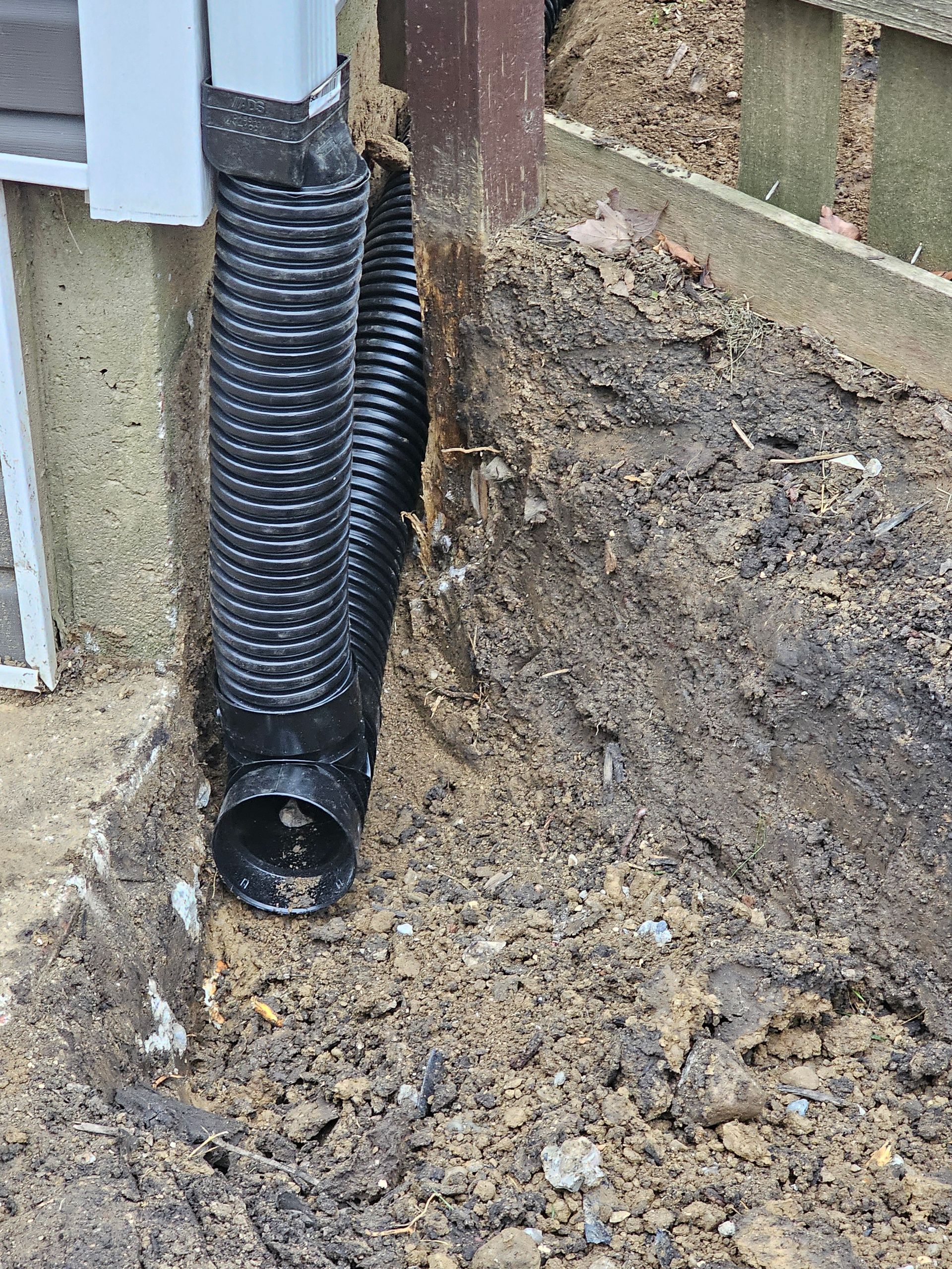 A black drain pipe is sitting in the dirt next to a house.