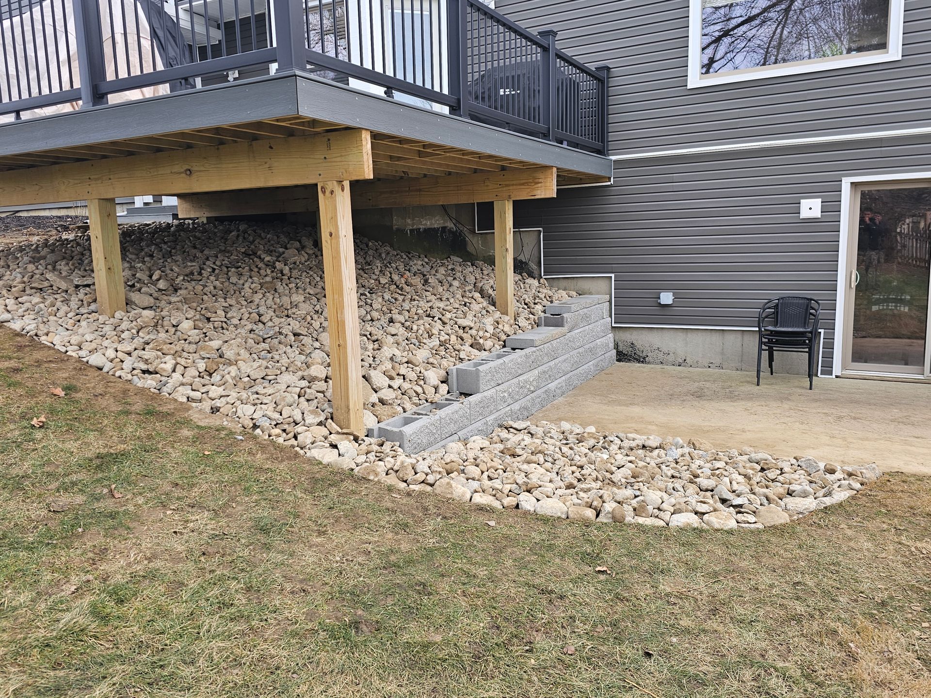 A deck is sitting on top of a rocky hill next to a house.
