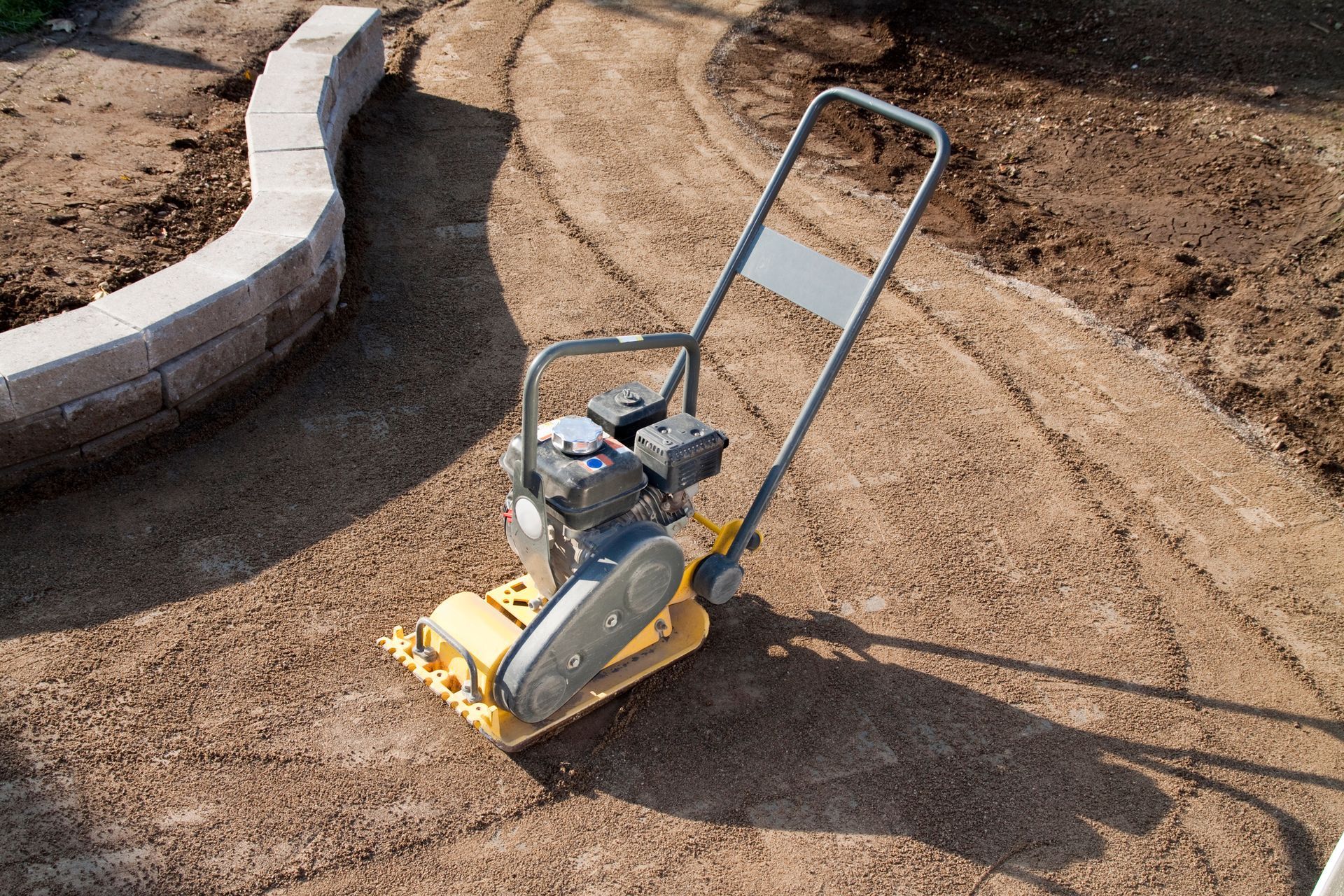 A yellow vibratory plate compactor is sitting on top of a dirt field.
