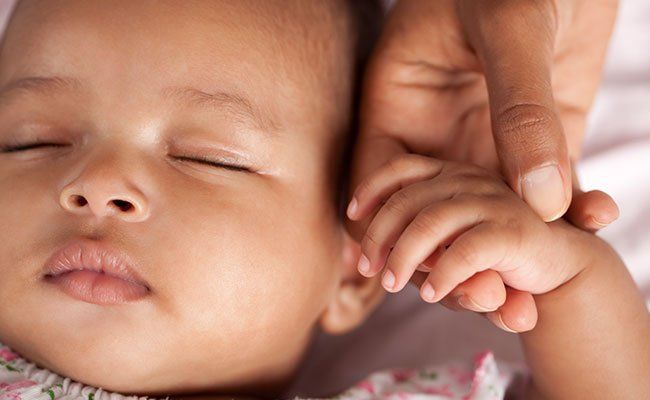 sleeping baby holding hands with an adult