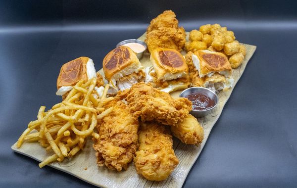 Fries topped with orange buffalo chicken, creamy sauce, and crunchy toppings in a black takeout container.