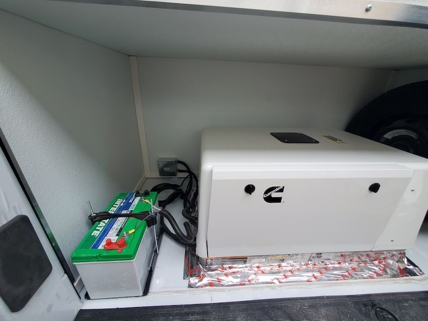 Two batteries and a generator inside a white compartment of a vehicle.