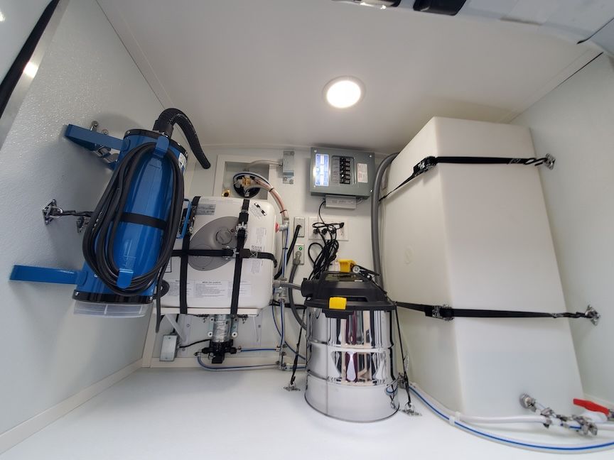 Interior of a van with cleaning equipment; blue machine, white tank, vacuum, electrical panel.