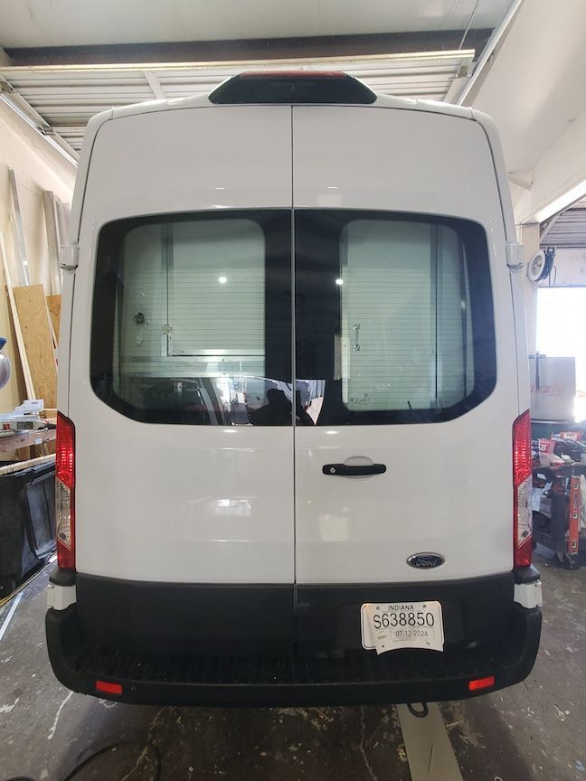 Rear view of a white van with black trim, windows, and a rear door handle, parked inside a building.
