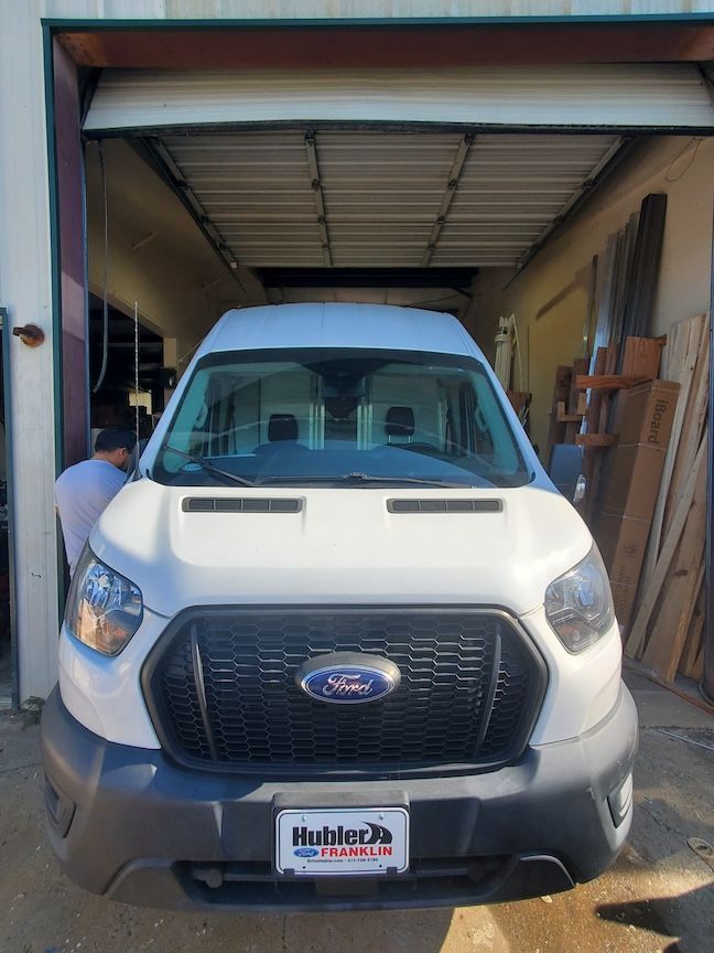 White Ford Transit van parked inside a garage; person in white shirt on the left.