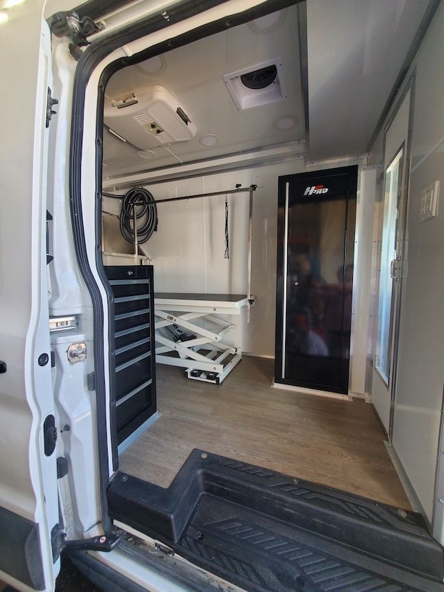 Interior of a white grooming van with grooming equipment, including a grooming table and cabinets.