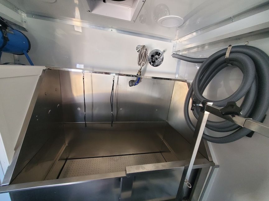 Interior of a pet grooming trailer with a stainless steel tub, hose, and ventilation system.