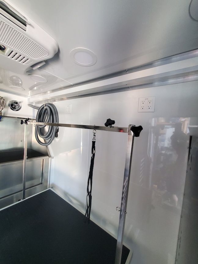 Interior of a dog grooming trailer with a grooming table, overhead lighting, and hose.