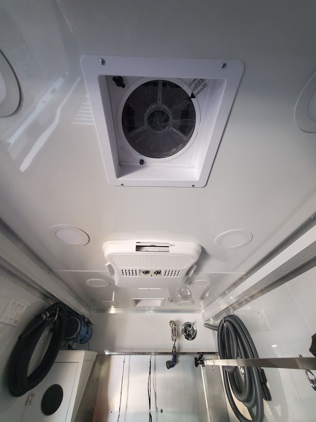 White interior of a vehicle with a ceiling vent, air conditioning unit, and various other objects mounted.