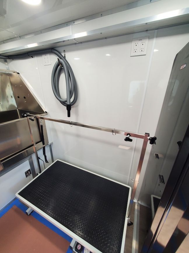 Dog grooming table inside a mobile grooming van. Includes hose, electrical outlet, and metal arm.