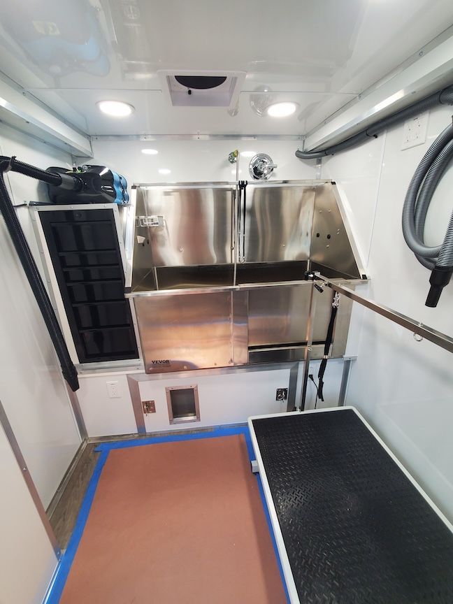Interior of a mobile pet grooming van with stainless steel tubs, grooming table, and storage.
