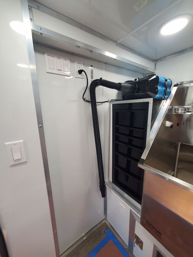 Interior view of a food truck with ventilation system and stainless steel counter. White walls with electrical outlet.