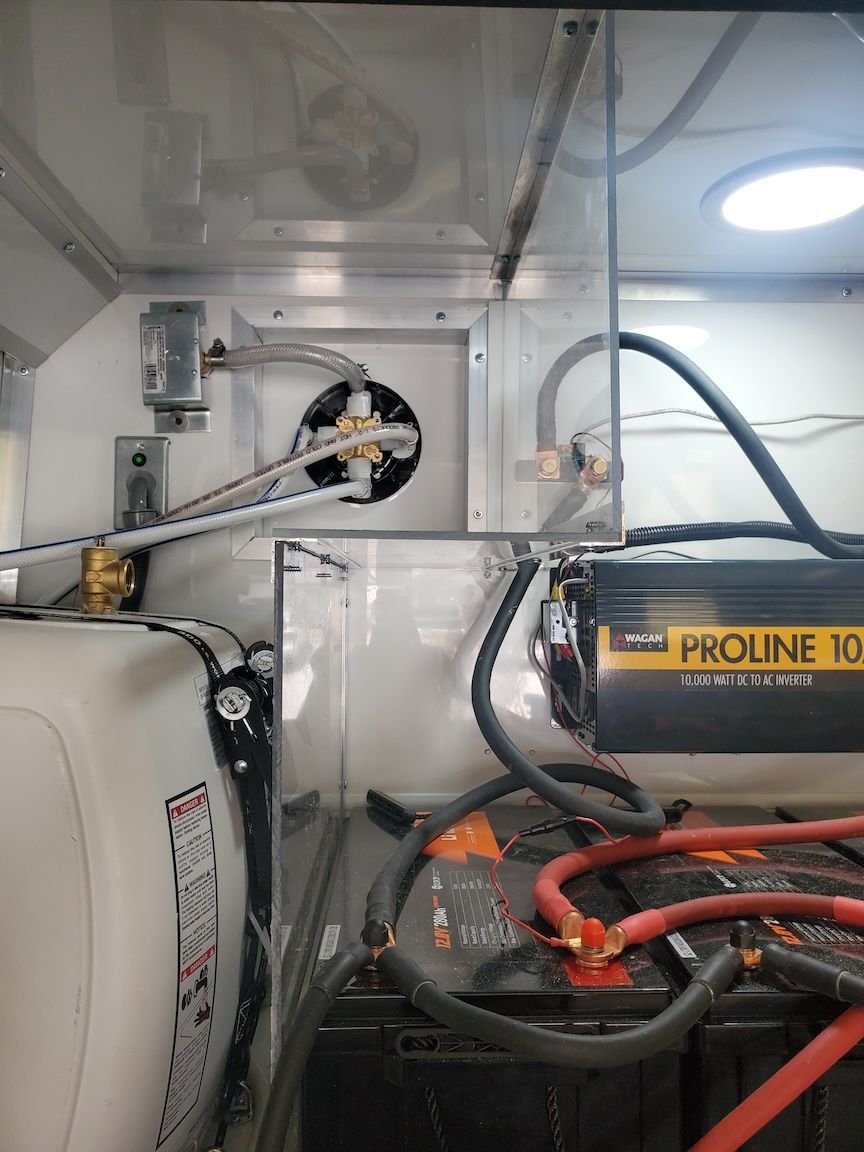 Interior of a vehicle, showing battery and electrical components near a water tank.