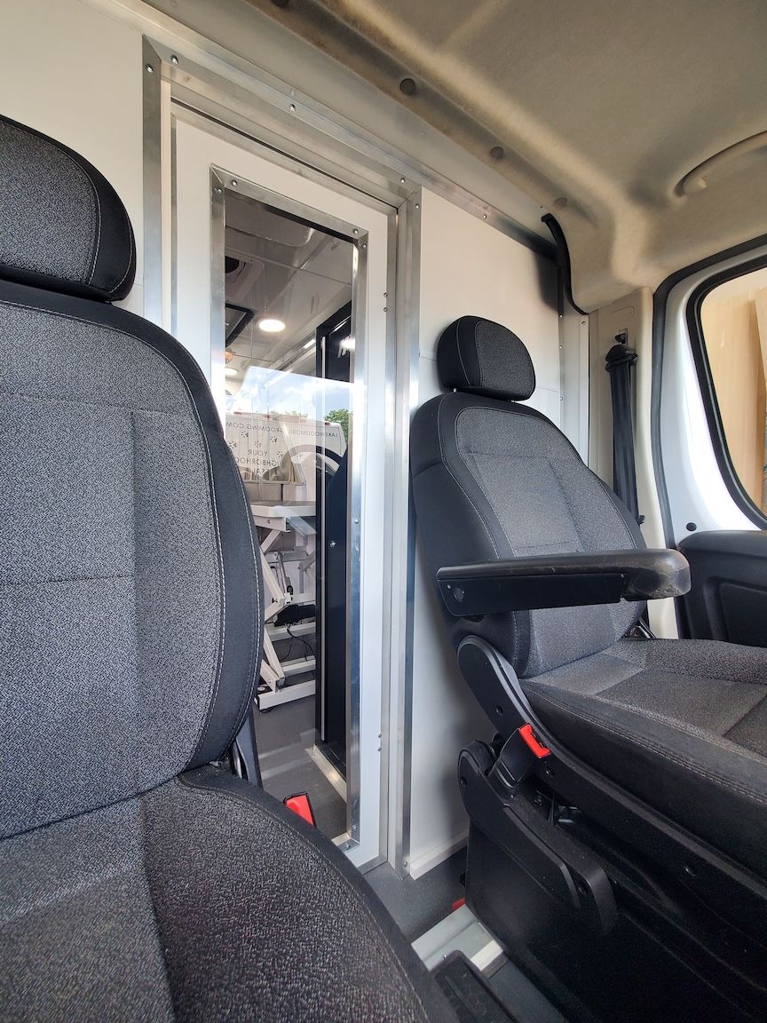 Interior of a van, showing two gray upholstered seats facing a doorway with a clear window.