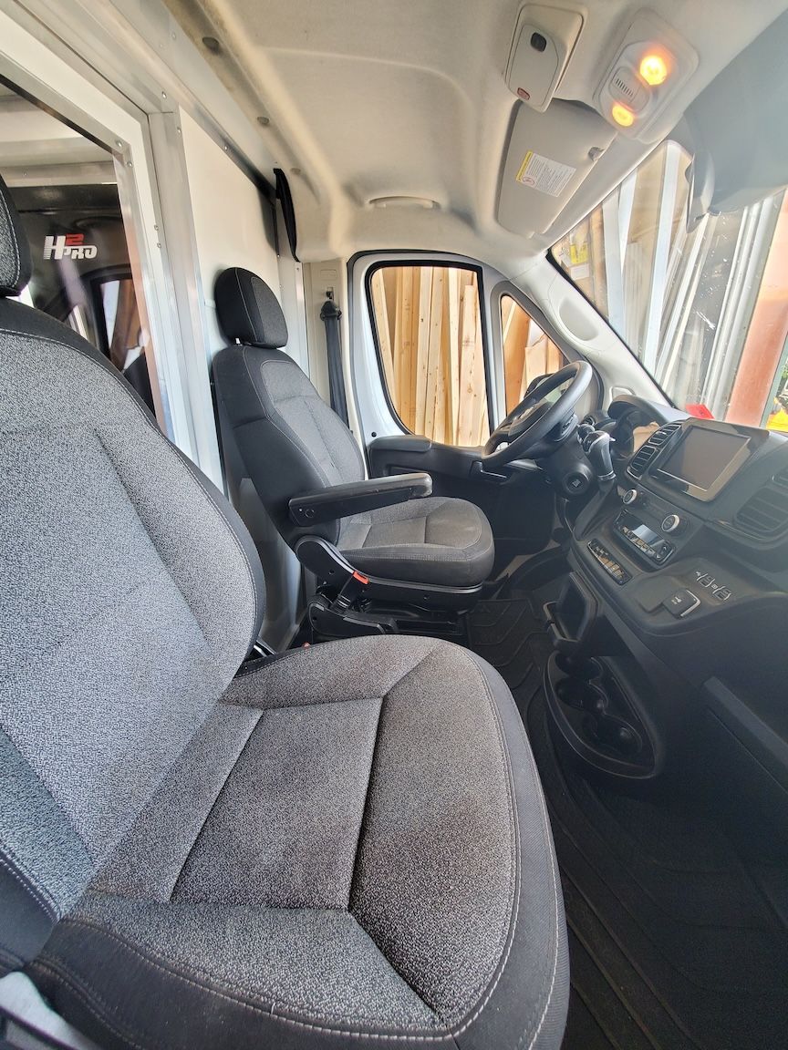 Interior of a van showing driver's seat, dashboard, and open door to the exterior. Gray and black.