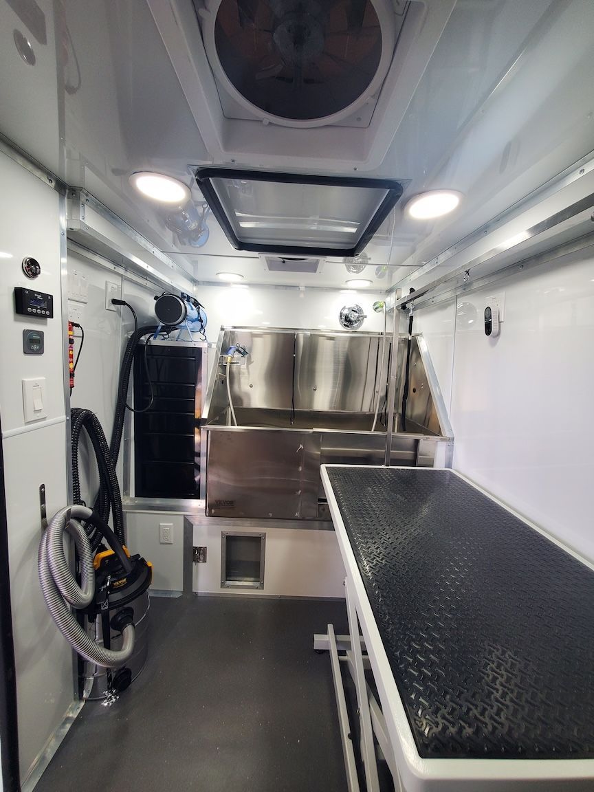 Interior of a white pet grooming van, showing stainless steel grooming stations and a black table.