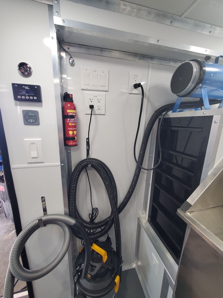 Interior of a utility trailer with electrical outlets, vacuum hose, and a fire extinguisher.