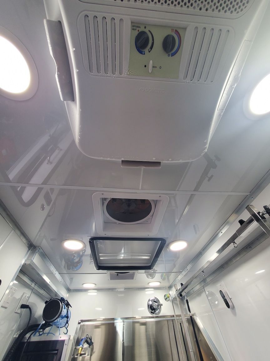 White interior of a vehicle with air conditioning unit, ceiling lights, and medical equipment.