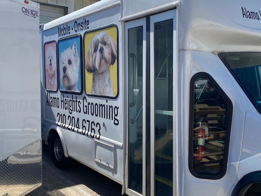 White mobile dog grooming van with dog portraits and business info.