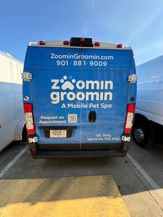 Blue Zoomin' Groomin' mobile pet spa van with logo, website, and phone number.