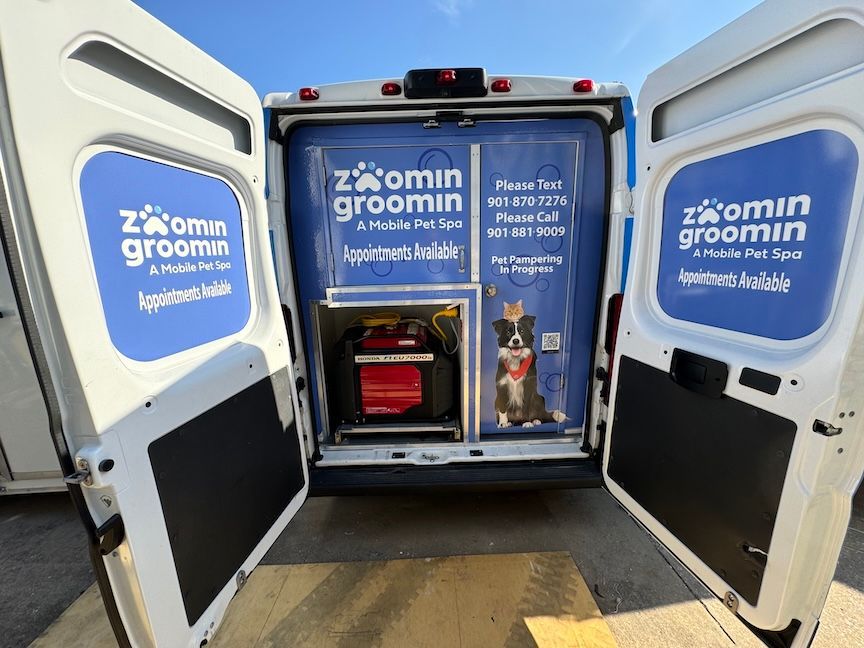 Rear view of a mobile pet grooming van with open doors, blue branding, and a red generator.