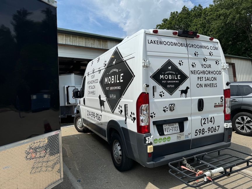 White mobile pet grooming van with black graphics, parked outdoors.