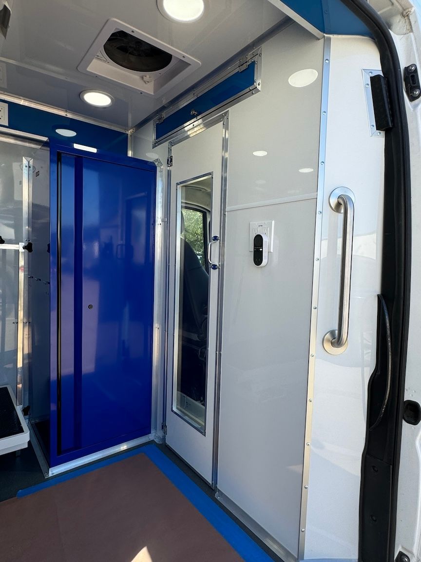 Interior of a white ambulance, showing a blue cabinet and sliding door with a silver handle.