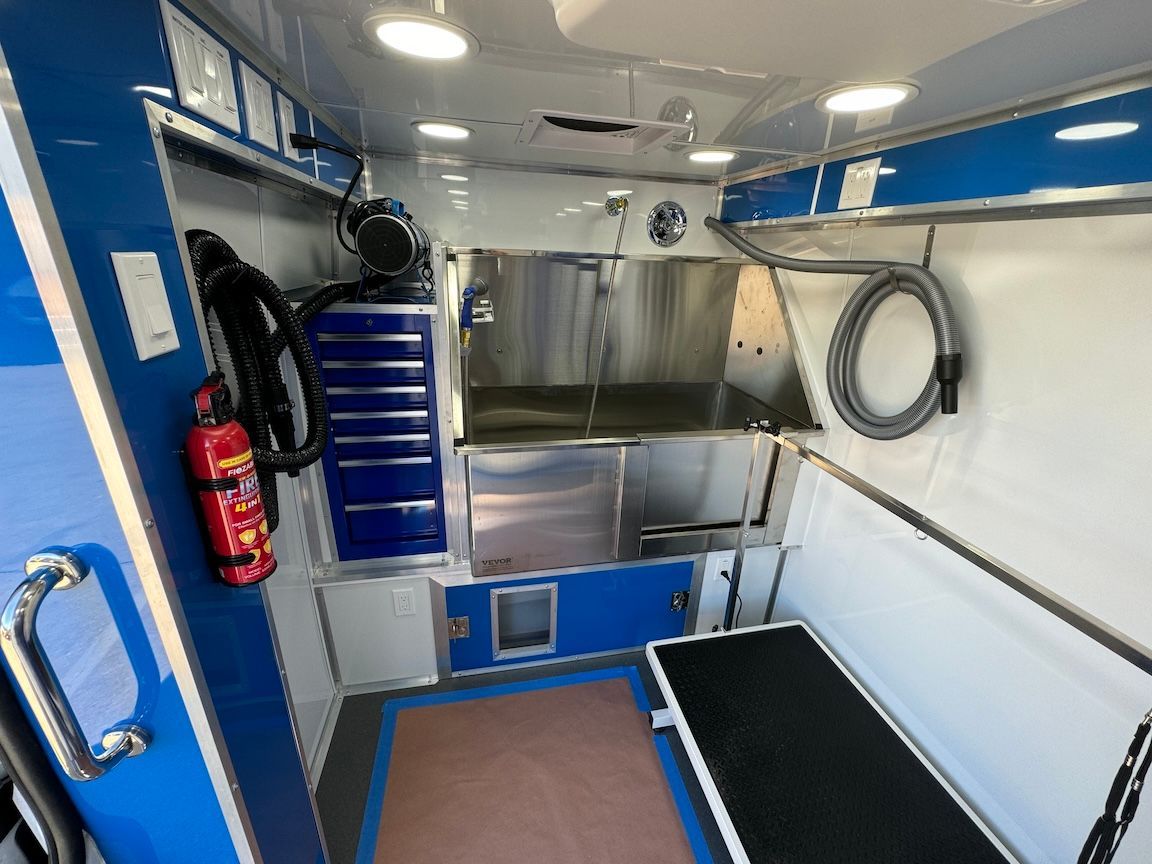 Interior of a mobile dog grooming van: stainless steel tub, blue and white accents, grooming table.