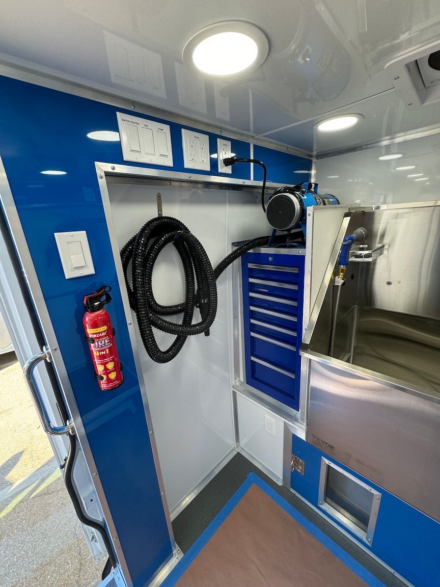 Interior of a blue and white mobile grooming vehicle with a hose, tool chest, and fire extinguisher.