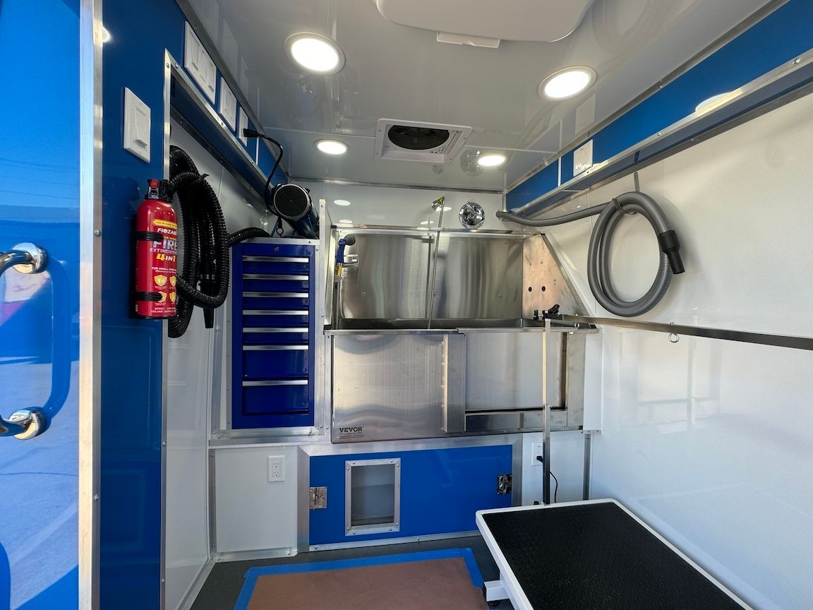 Interior of a mobile pet grooming van, featuring grooming station, tools, and storage.