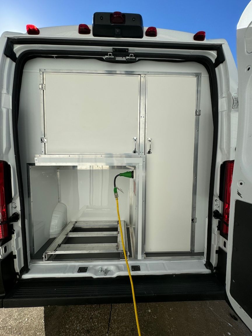 Open white van interior with a refrigeration unit, containing shelving and a door.