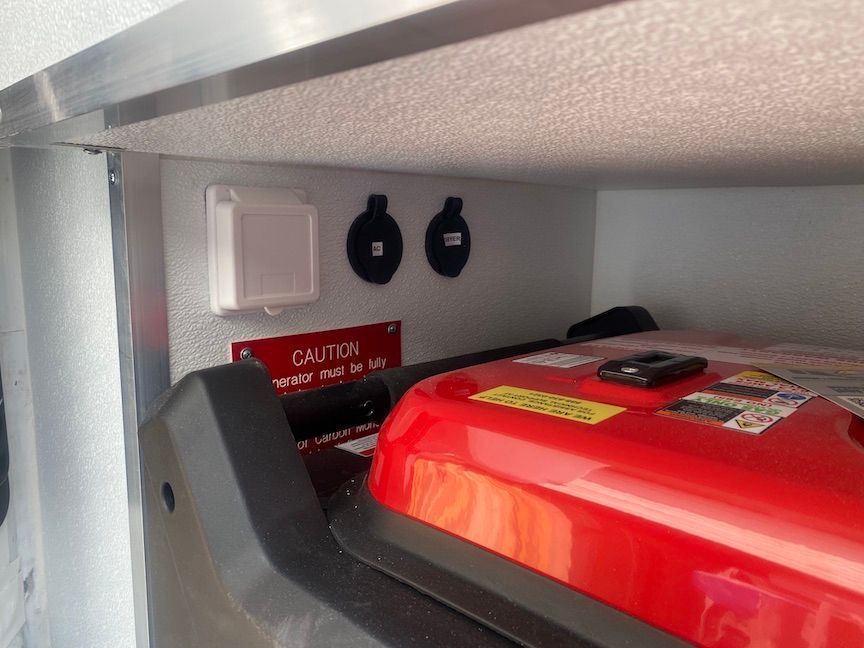 A red generator is sitting under a shelf with a caution sign on it.