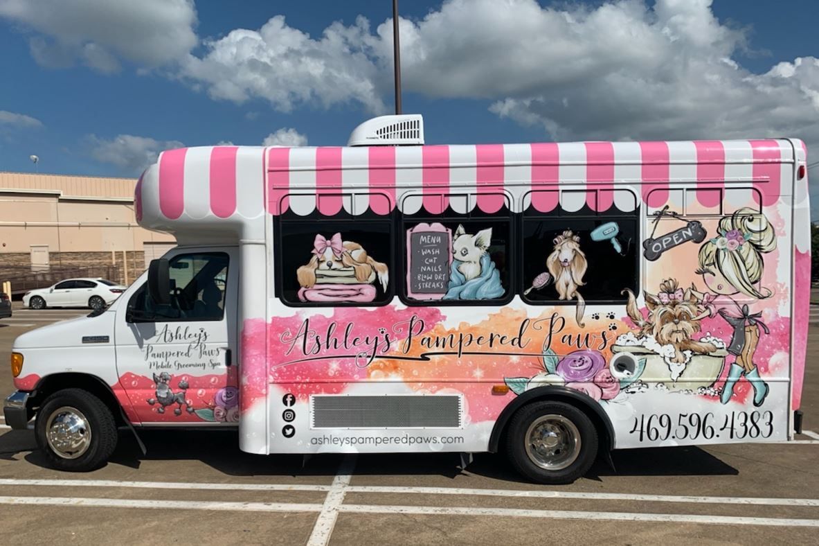 A pink and white food truck is parked in a parking lot.