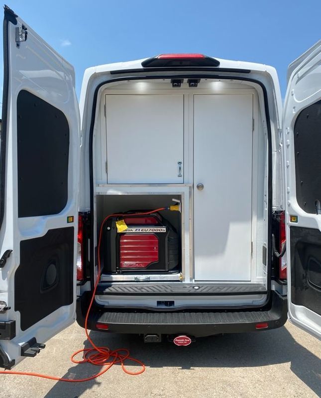 A white van with the doors open and a generator in the back
