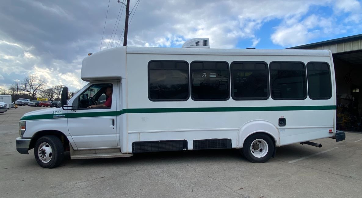 A white bus with green stripes is parked in a parking lot.