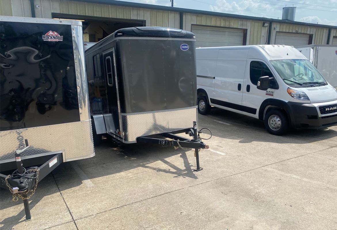 A white van is parked next to a trailer in a parking lot.