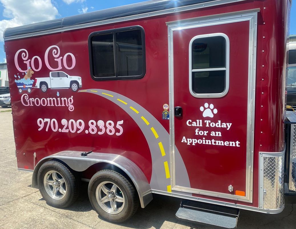 A red trailer for go go grooming is parked in a parking lot.