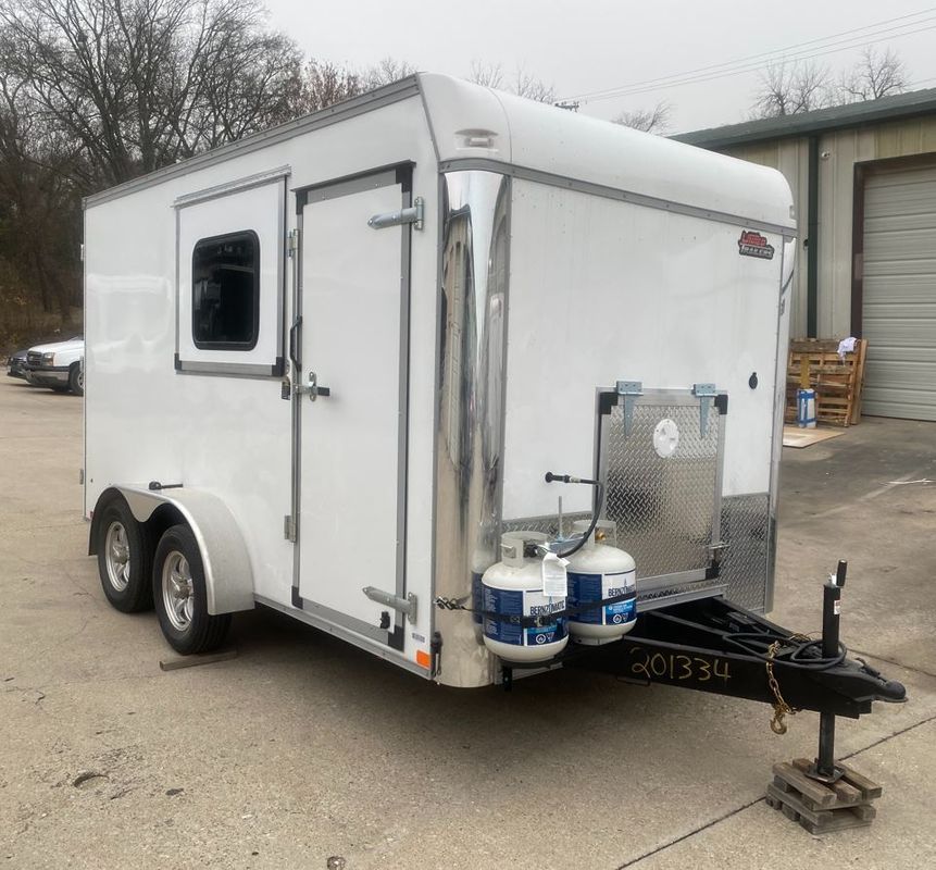 A white trailer with two propane tanks attached to it is parked in a parking lot.