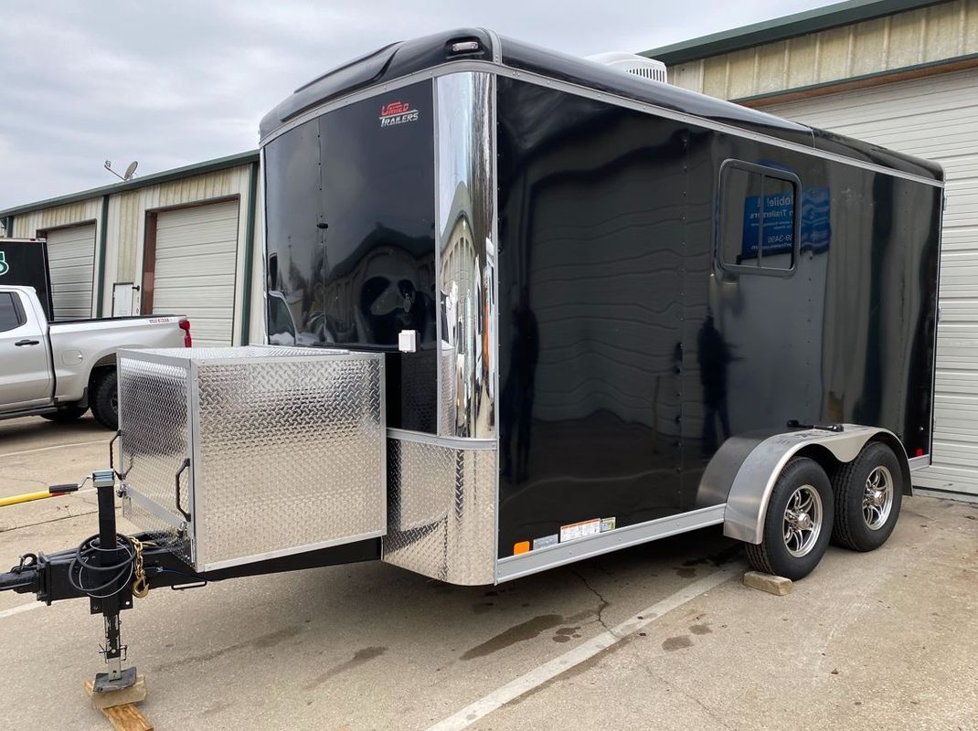 A black trailer is parked in a parking lot next to a truck.
