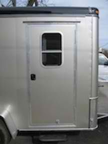 A silver trailer with a window is parked next to a truck.