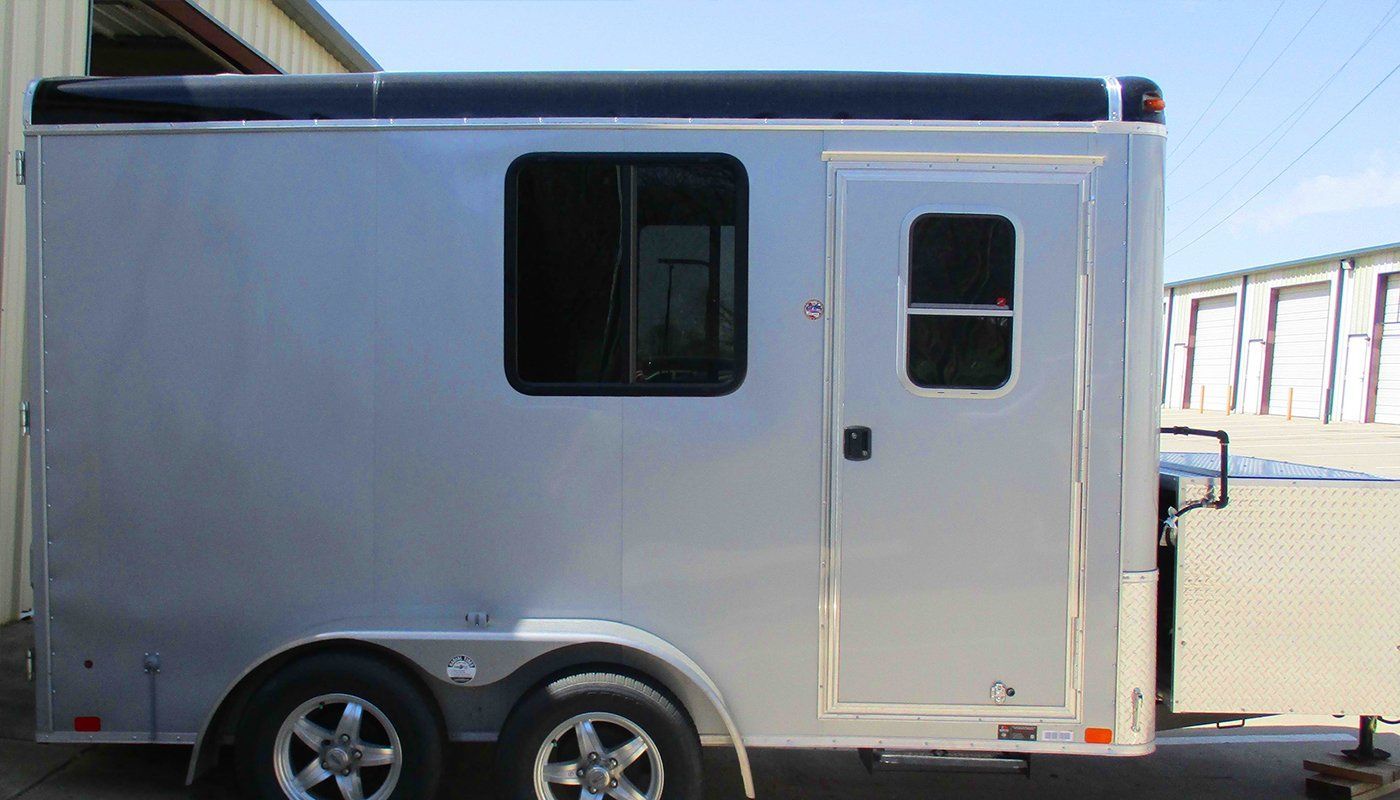 A white trailer with a black top is parked in front of a building.