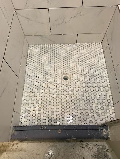A shower stall with white tiles and a black drain.