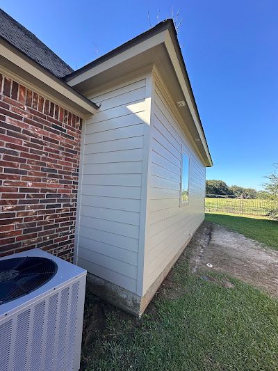 The side of a house with a brick wall and a white siding.
