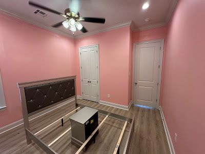 A bedroom with pink walls , a bed and a ceiling fan.