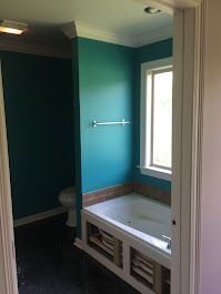 A bathroom with blue walls, a tub, a toilet, and a window.