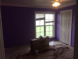 An empty room with purple walls and a ceiling fan.