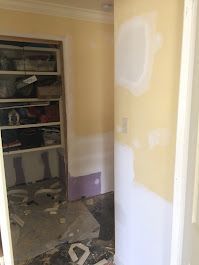 A room with yellow walls and white trim is being painted.