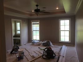 A room with a ceiling fan and two windows is being painted.
